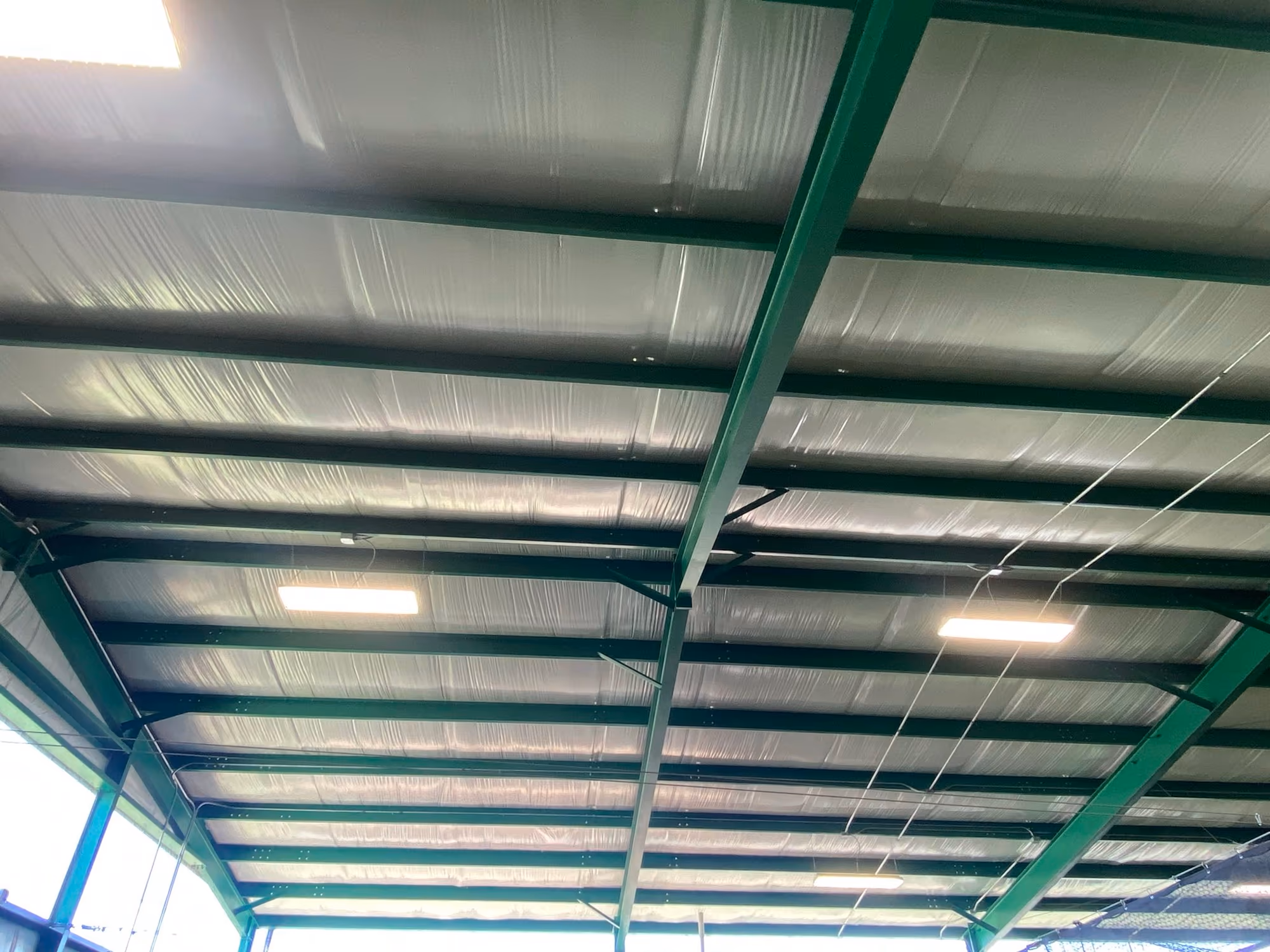 Looking up inside the Valley Springs Fitness Center — green-painted steel purlins and rafters carrying the white underside of the metal roof deck